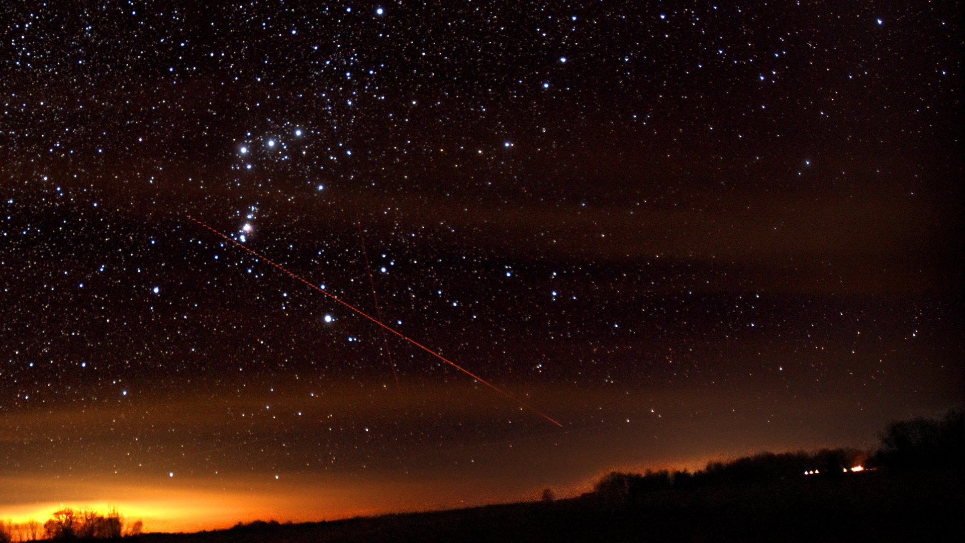Orion in a dark, star-filled sky above a treeline at night